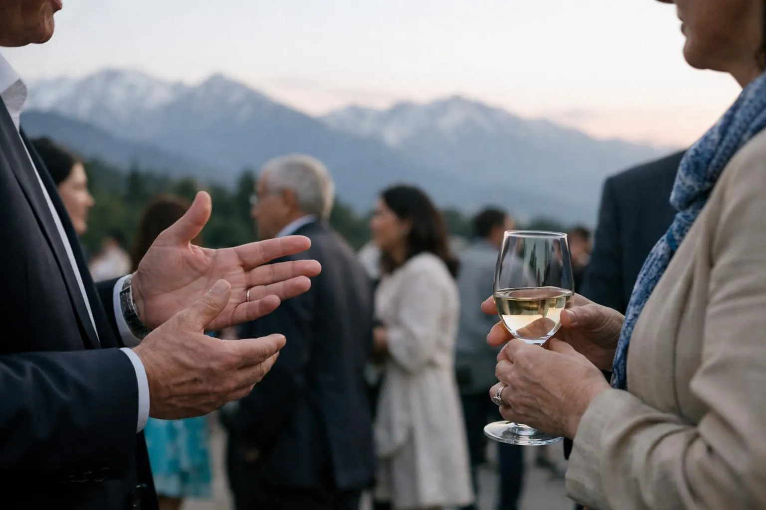 Groupe de personnes discutant et buvant du vin devant un paysage montagneux.